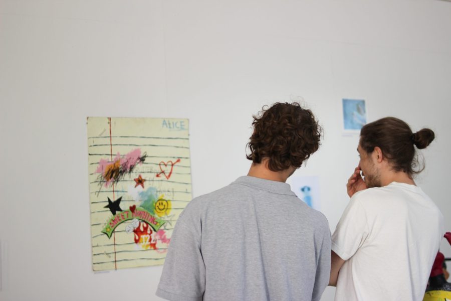 People look at artworks on wall in Fledglings exhibition