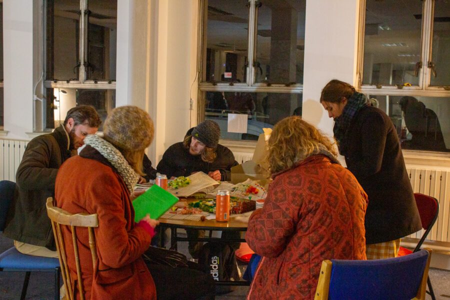 A group of people sat around a table taking part in tufting and talking at St Anne's House.