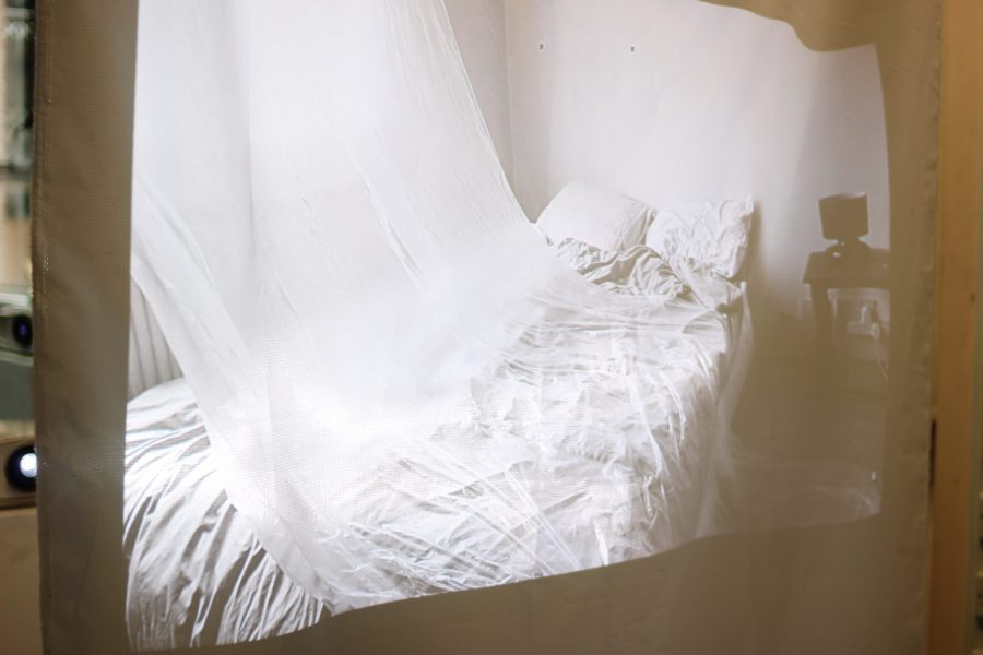 A projection artwork for Confine + Escape or a bed with a sheer curtain blowing over it.