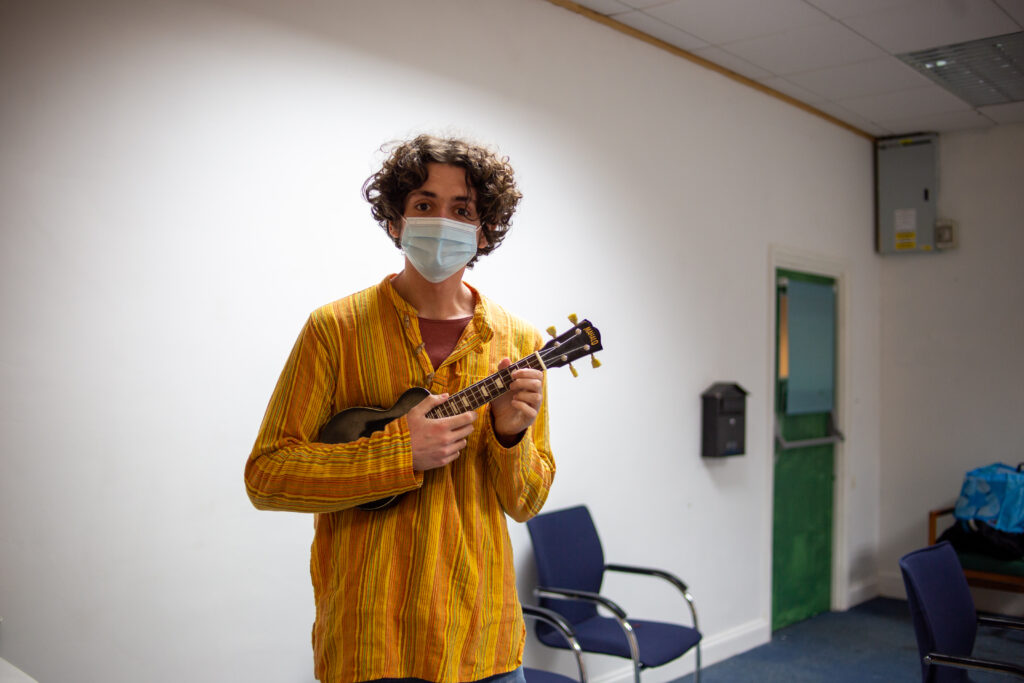 A person holding a ukulele and looking at the camera for a workshop 