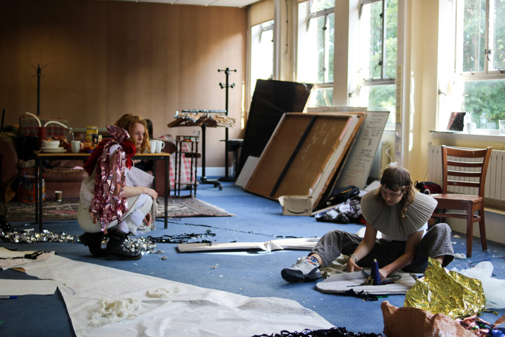 Two young people sitting on the ground cutting and stitching fabrics together
