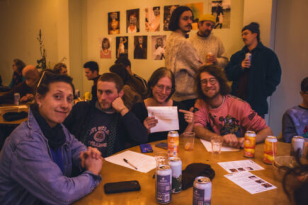 A group of people sitting and smiling at the camera. The woman in the middle is holding up the quiz sheet and pointing.