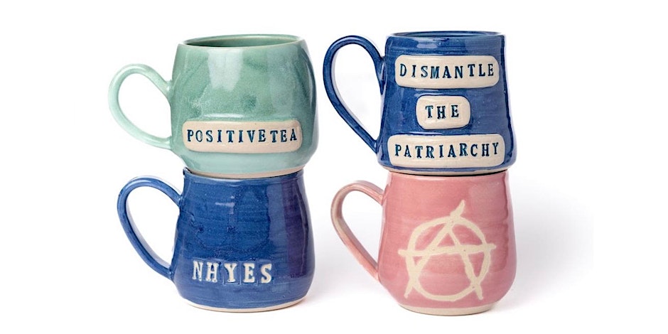 Four mugs, with two balancing on top of the other two, one is green and says 'positivetea', the second is blue and says 'dismantle the patriarchy' the third is blue and says 'nhyes' and the fourth is a pink colour with a symbol on.