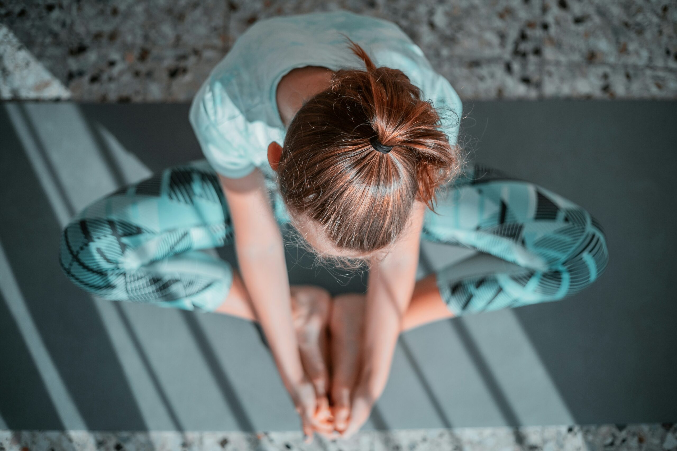 An image of a brunette woman sat in a yoga position form above on the matt.