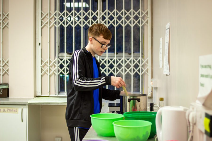 A young person stirring a pot in the kitchen whilst making dinner at St Anne's House.