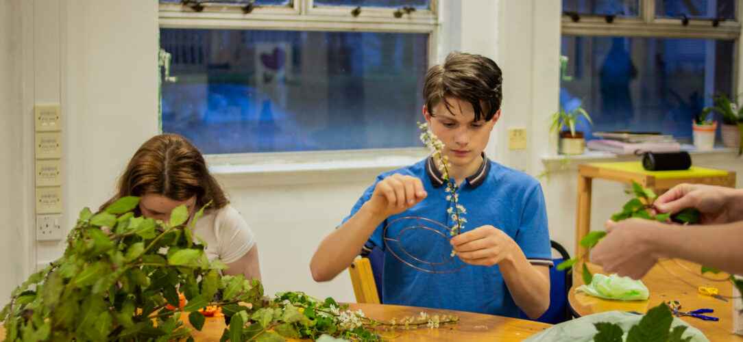 A young boy in a blue shirt making a wreath with flowers at St Anne's Young People - Open Access Sessions in March 2024.