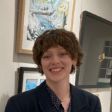 A woman with short brown hair, smiling in front of artwork.