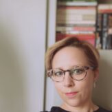 A woman posing for a headshot, wearing glasses.