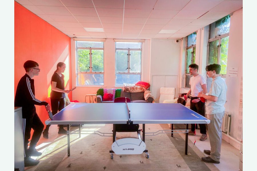 Four people laughing and playing ping pong at St Anne's House.