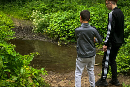 Two young people throwing pebbles into a stream in the woods.