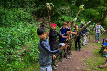 A group of people stood in a line holding large wooden sticks in the woods.